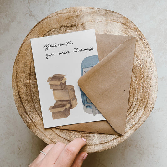 Klappkarte mit blauem Bulli, neben welchem vier gestapelte Umzugskartons stehen. Lettering: ,,Glückwunsch zum neuen Zuhause''