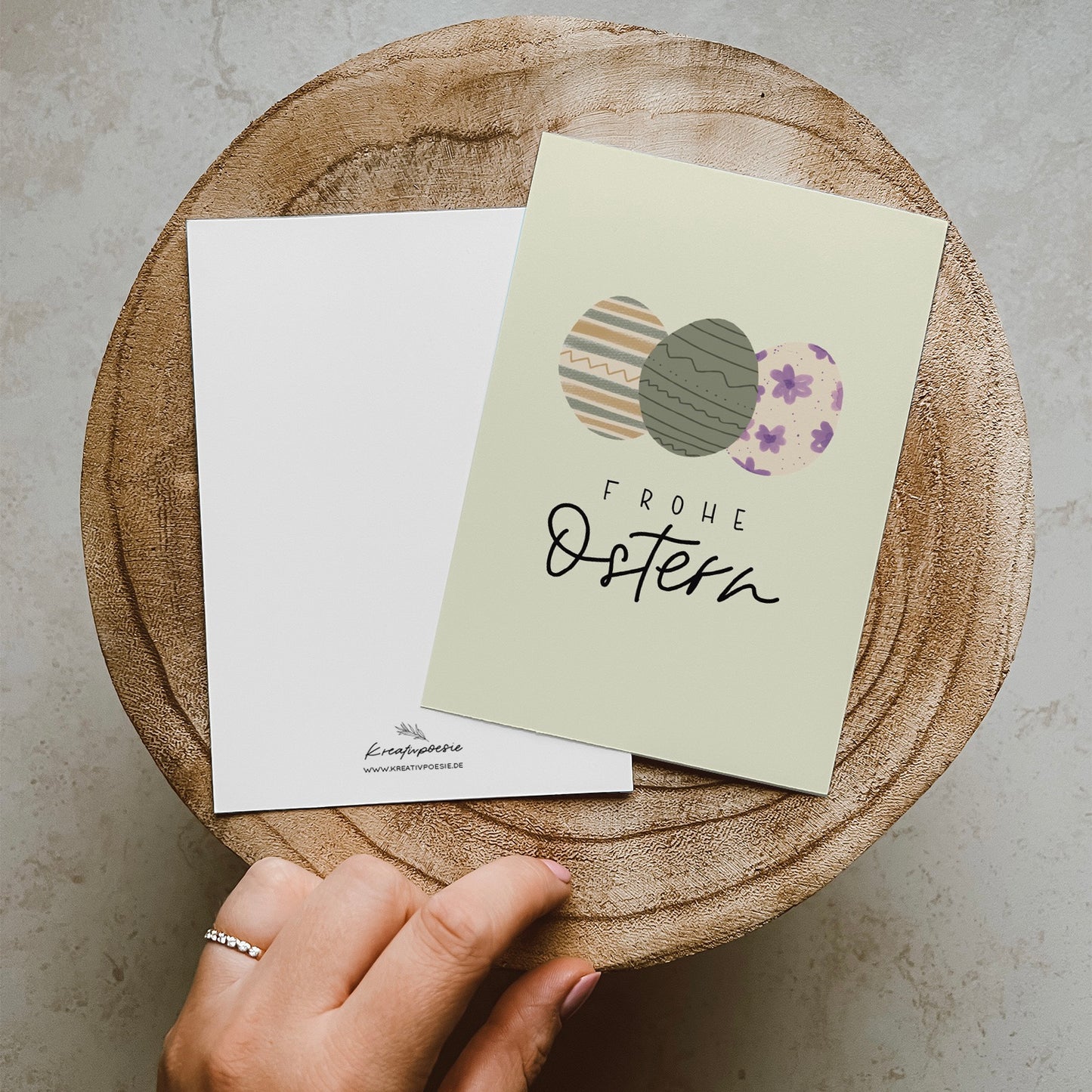 Postkarte im Hochformat, Abgebildet sind drei bunte Eier in Pastellfarben. Der Hintergrund ist Pastellgrün. Auf der Karte steht ein Lettern mit dem Text Frohe Ostern