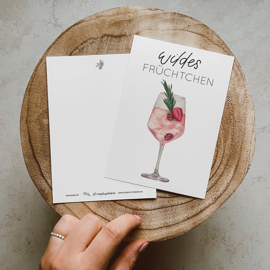 Postkarte DIN A6, Hochformat, gedruckt in Deutschland. Auf dieser Karte befindet sich ein Weinglas mit Früchten und ein rosa gefärbtes Getränk, welches an Lille Wild Berry erinnern soll. Über ihm befindet sich ein Lettering ,,wildes Früchtchen''.
