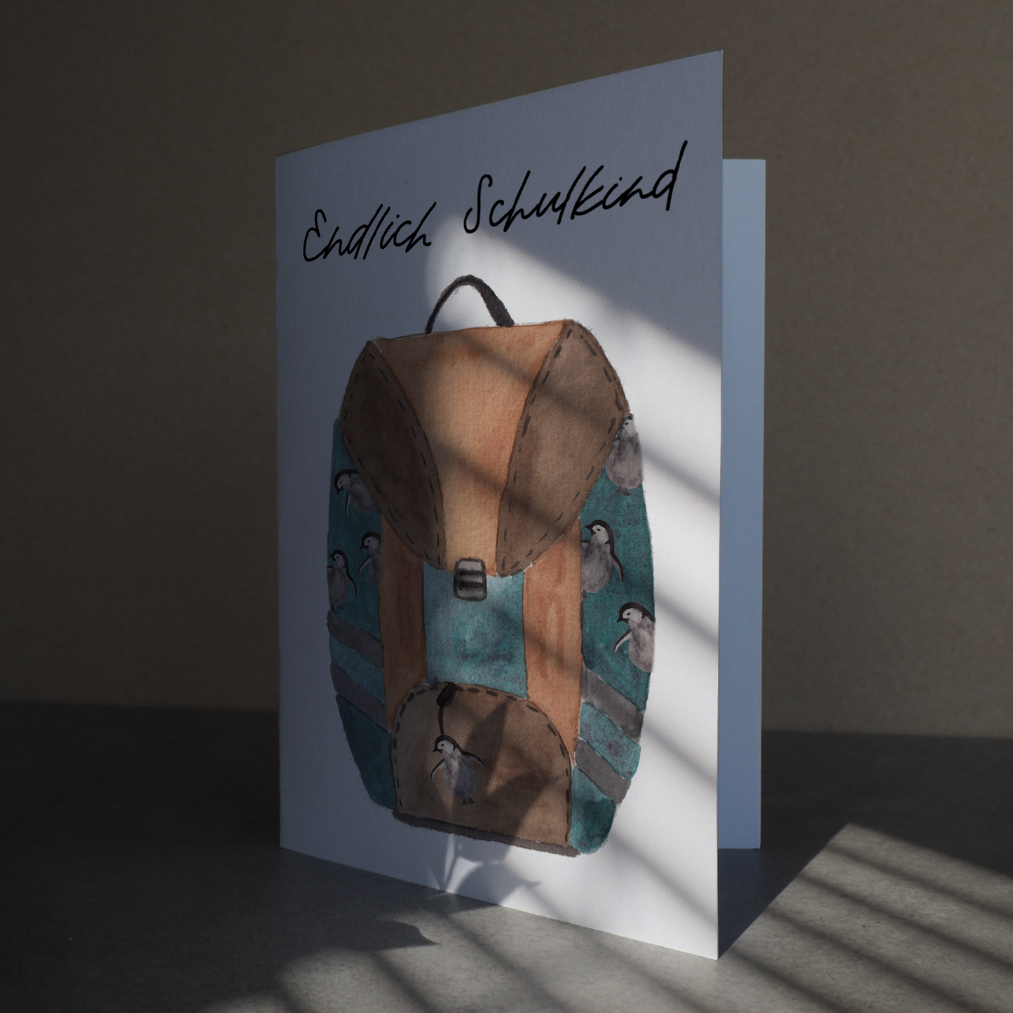 Klappkarte zur Einschulung auf der ein Schulrucksack mit Pinguinen abgebildet ist. Aufschrift ,,Endlich Schulkind''