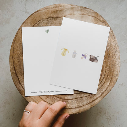 Postkarte im Hochformat. Anlass: Baby, Geburt, Zwillinge, Babyparty, Glückwunsch. Auf der Karte befinden sich vier typische Baby Gegenstände, welche alle mittig von links nach rechts angeordnet sind. Ganz links befindet sich ein gelber Babybody. Daneben eine Milchflasche mit hellblauem Verschluss. Danach kommt ein lilaner Schnuller und ganz rechts befindet sich ein brauner Schnürschuh. Die Karte bietet oben und unten genug Platz für Texte.