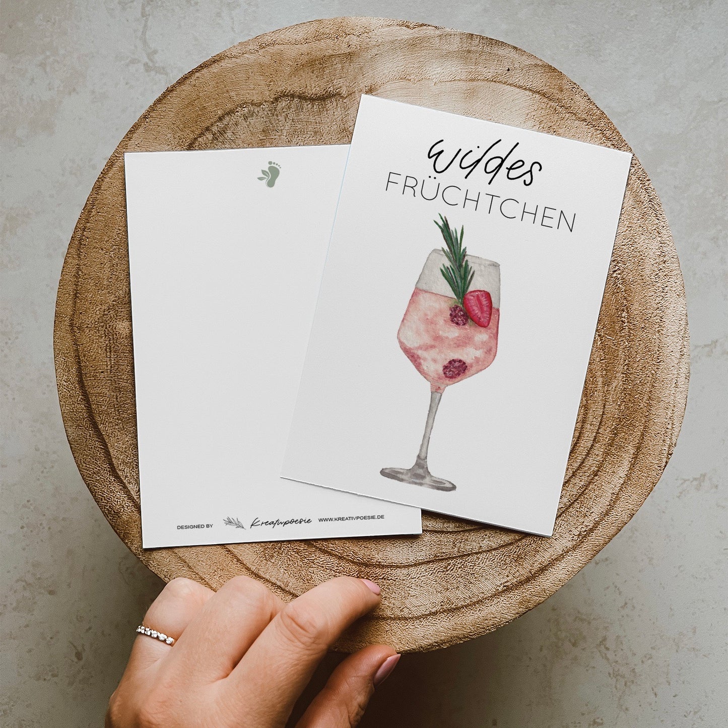 Postkarte DIN A6, Hochformat, gedruckt in Deutschland. Auf dieser Karte befindet sich ein Weinglas mit Früchten und ein rosa gefärbtes Getränk, welches an Lille Wild Berry erinnern soll. Über ihm befindet sich ein Lettering ,,wildes Früchtchen''.