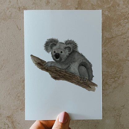 Postkarte DIN A6, Hochformat, gedruckt in Deutschland. Auf dieser Karte befindet sich ein junger Koala, welcher sich gemütlich einen Baumstamm klammert.