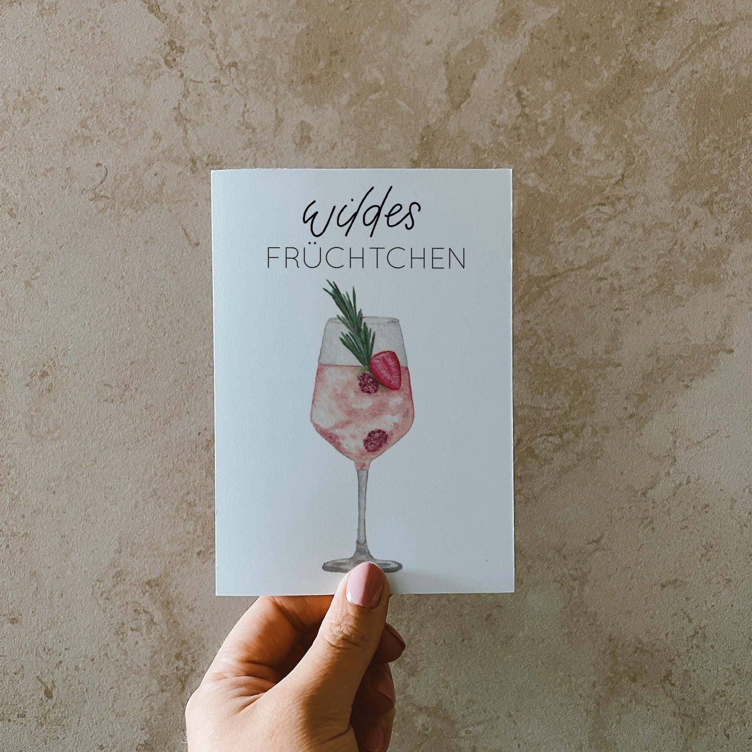 Postkarte DIN A6, Hochformat, gedruckt in Deutschland. Auf dieser Karte befindet sich ein Weinglas mit Früchten und ein rosa gefärbtes Getränk, welches an Lille Wild Berry erinnern soll. Über ihm befindet sich ein Lettering ,,wildes Früchtchen''.