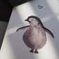 Grau schwarzer Pinguin mit abstehenden Flügeln, nach links schauend mit einem Herz über ihm. Gedruckt auf Recyclingpapier in Deutschland. Nahansicht.