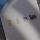 Postkarte im Hochformat. Nahansicht. Anlass: Baby, Geburt, Zwillinge, Babyparty, Glückwunsch. Auf der Karte befinden sich vier typische Baby Gegenstände, welche alle mittig von links nach rechts angeordnet sind. Ganz links befindet sich ein gelber Babybody. Daneben eine Milchflasche mit hellblauem Verschluss. Danach kommt ein lilaner Schnuller und ganz rechts befindet sich ein brauner Schnürschuh. Die Karte bietet oben und unten genug Platz für Texte.