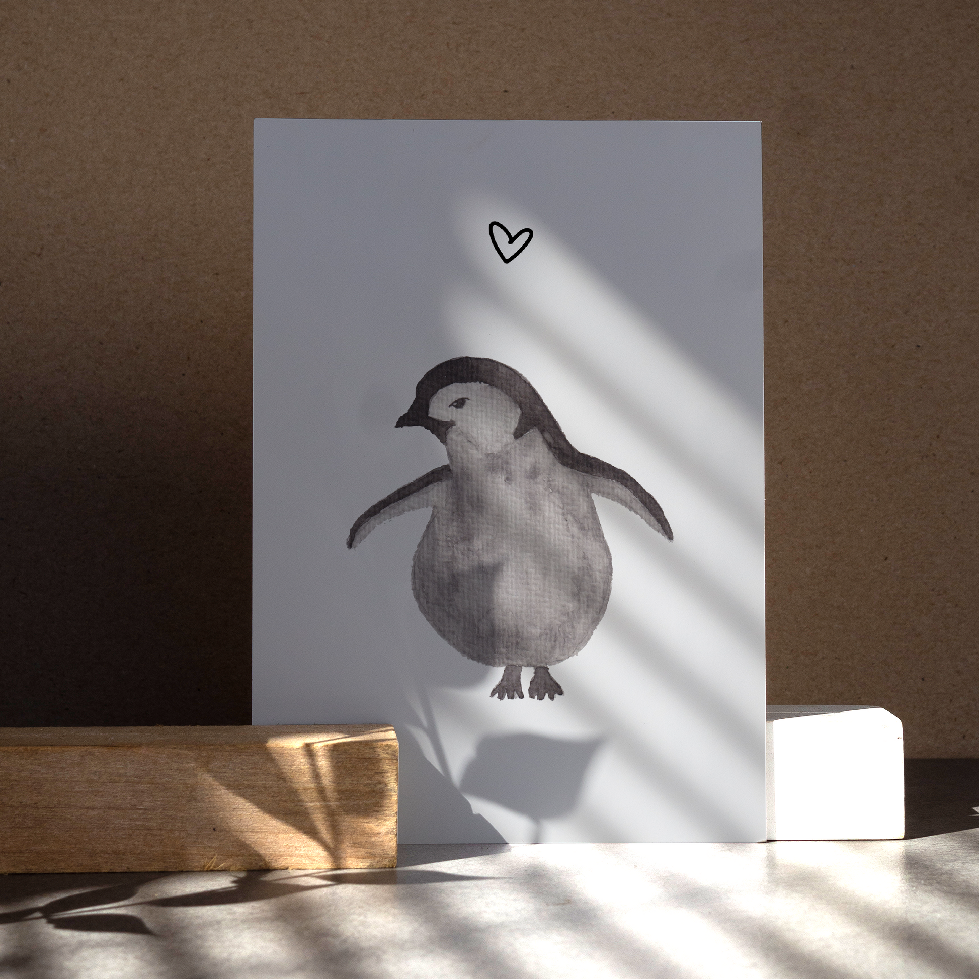 Grau schwarzer Pinguin mit abstehenden Flügeln, nach links schauend mit einem Herz über ihm.  Gedruckt auf Recyclingpapier in Deutschland.